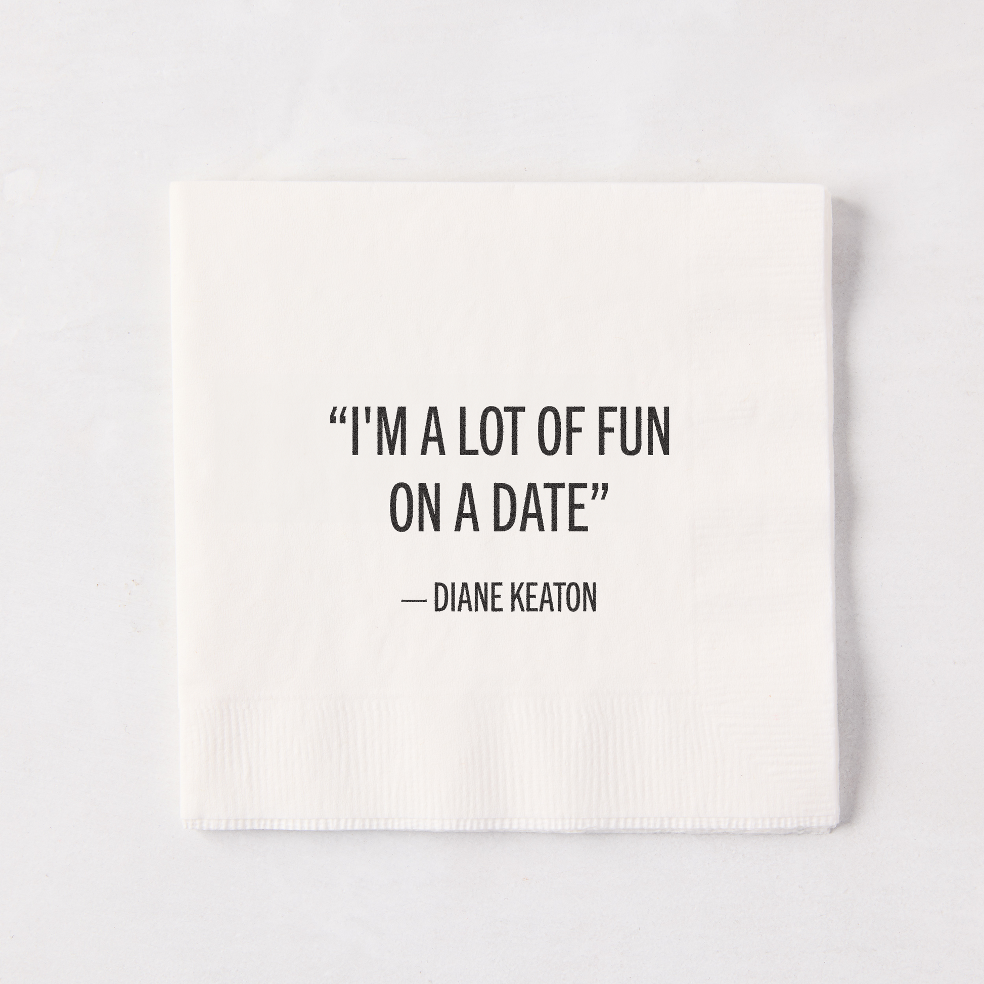 White 5.5" square paper cocktail napkin with "I'M A LOT OF FUN ON A DATE" - DIANE KEATON quote.