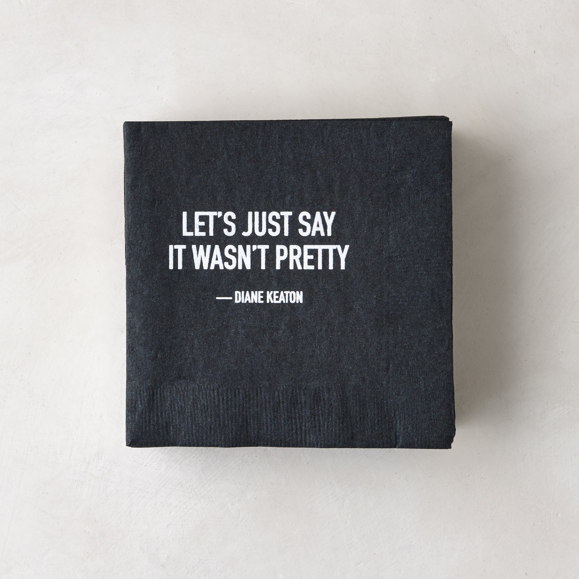 Black 5.5" square paper cocktail napkin with white "LET'S JUST SAY IT WASN'T PRETTY - DIANE KEATON" quote.