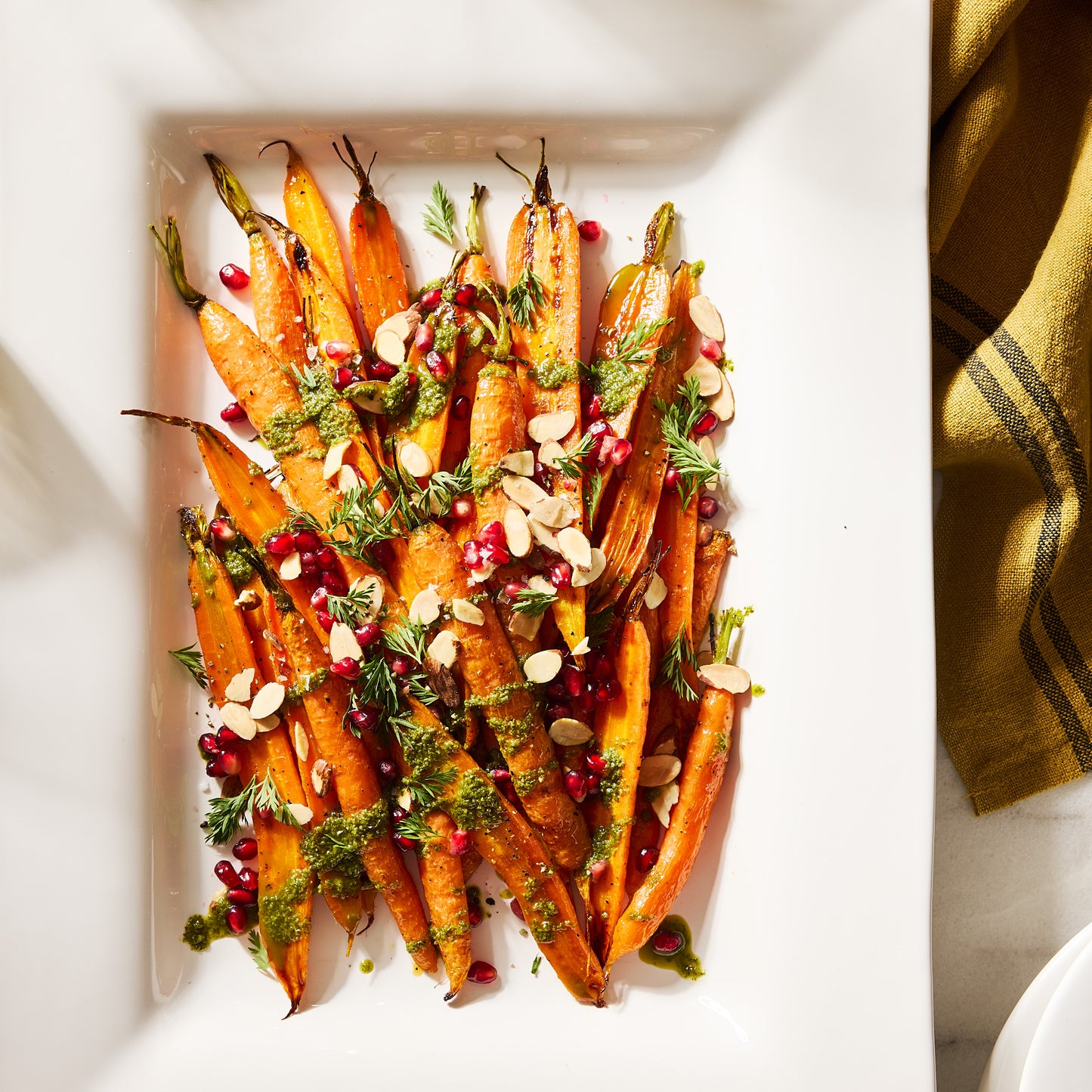 White rectangular ceramic serving platter with roasted carrots, pesto, pomegranate, and almonds.
