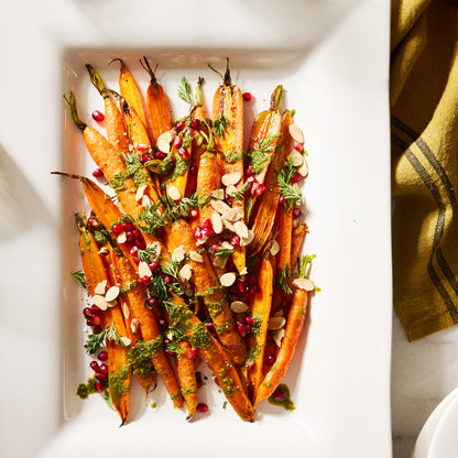 White rectangular ceramic serving platter with roasted carrots, pesto, pomegranate, and almonds.