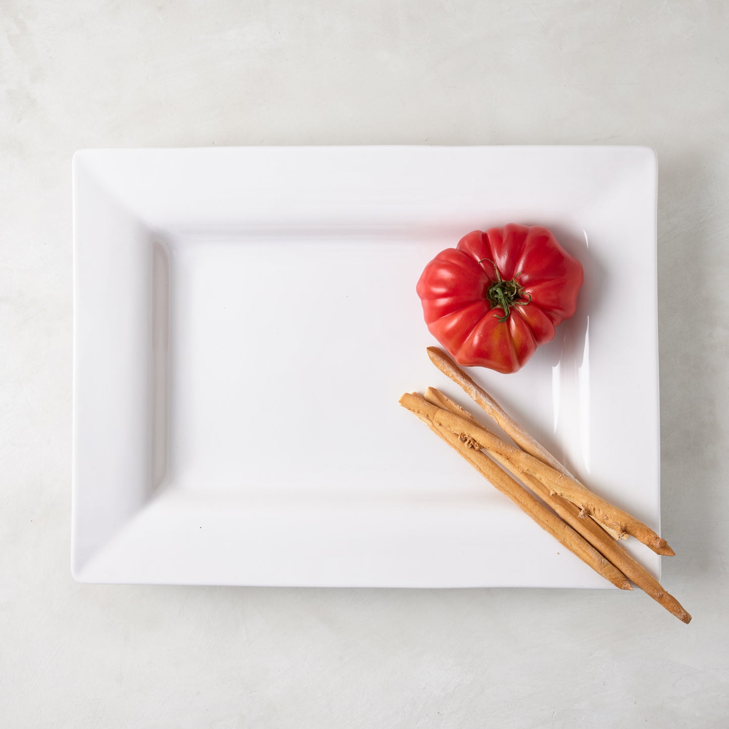 White ceramic "Keaton" large rectangular serving platter with a wide border, holding a red tomato and breadsticks.