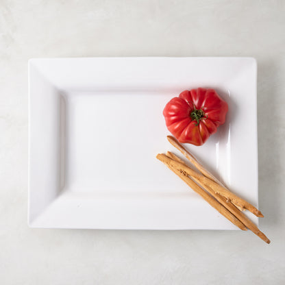 White ceramic "Keaton" large rectangular serving platter with a wide border, holding a red tomato and breadsticks.