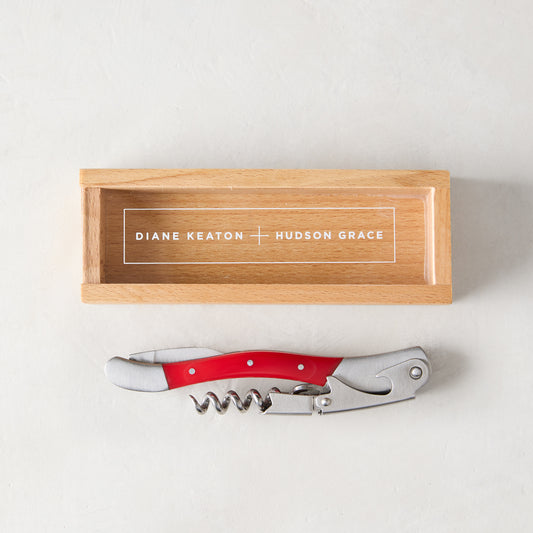 Diane Keaton + Hudson Grace "Keaton Red" wine corkscrew with a red resin handle and stainless steel tools, next to a branded wooden gift box.