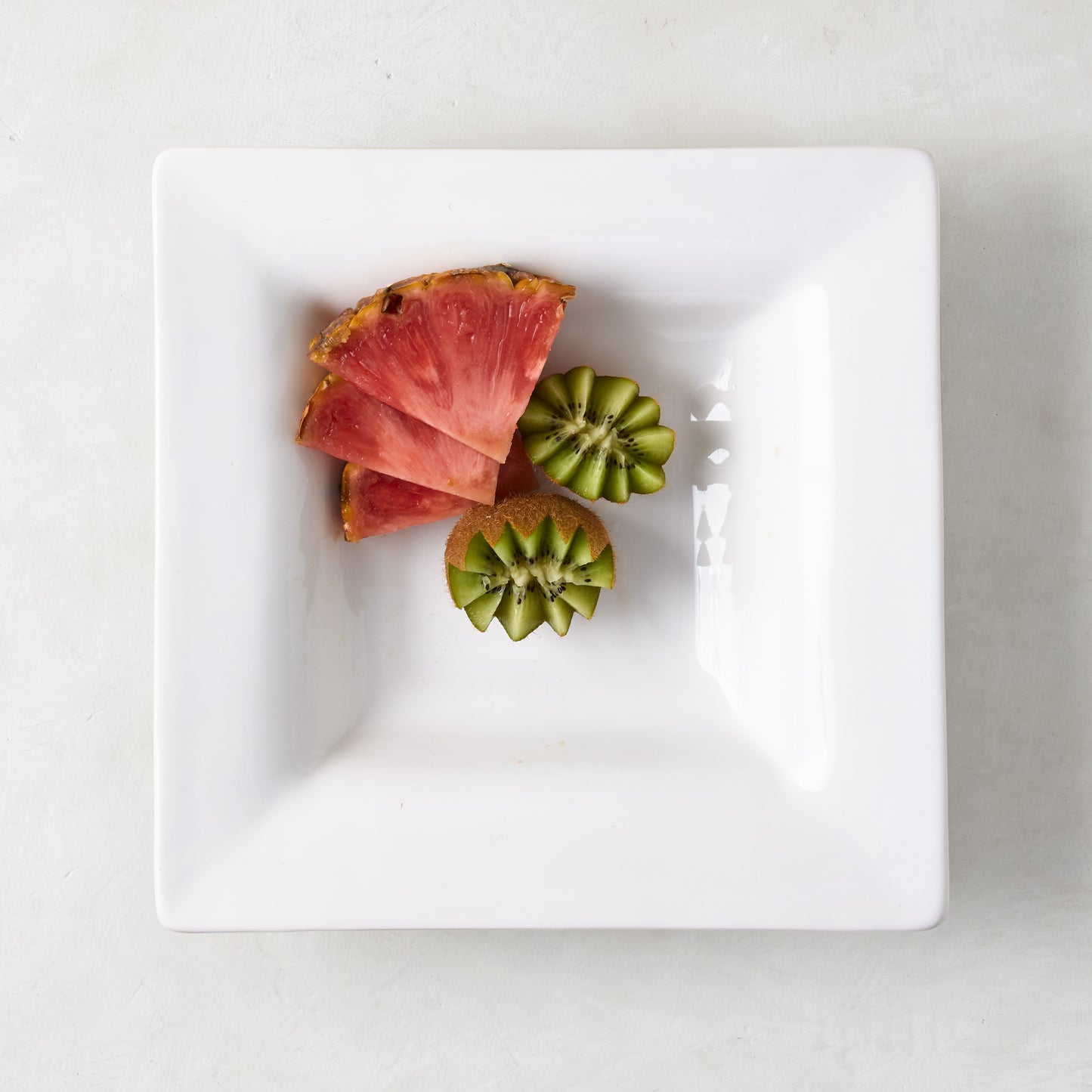 White ceramic "Keaton" small square serving platter with a wide border, holding sliced pineapple and kiwi.