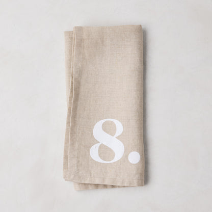 Diane Keaton + Hudson Grace Khaki Linen Numeric Napkin, folded, with a white number 8.