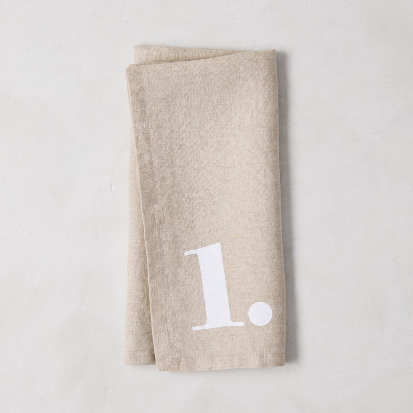 Diane Keaton + Hudson Grace Khaki Linen Numeric Napkin, folded, with a white number "1" design.