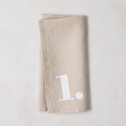 Diane Keaton + Hudson Grace Khaki Linen Numeric Napkin, folded, with a white number "1" design.