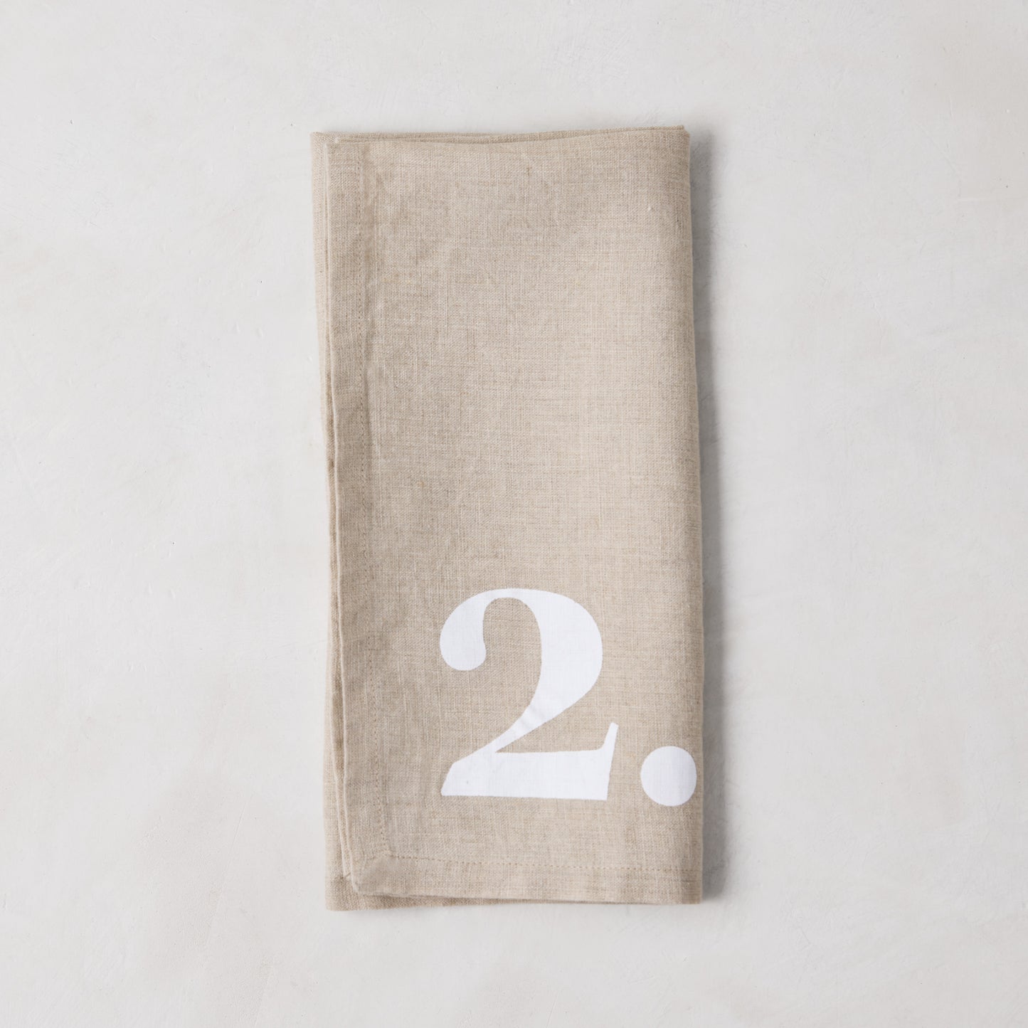 Diane Keaton + Hudson Grace Khaki Linen Numeric Napkin, folded, with a bold white number 2.