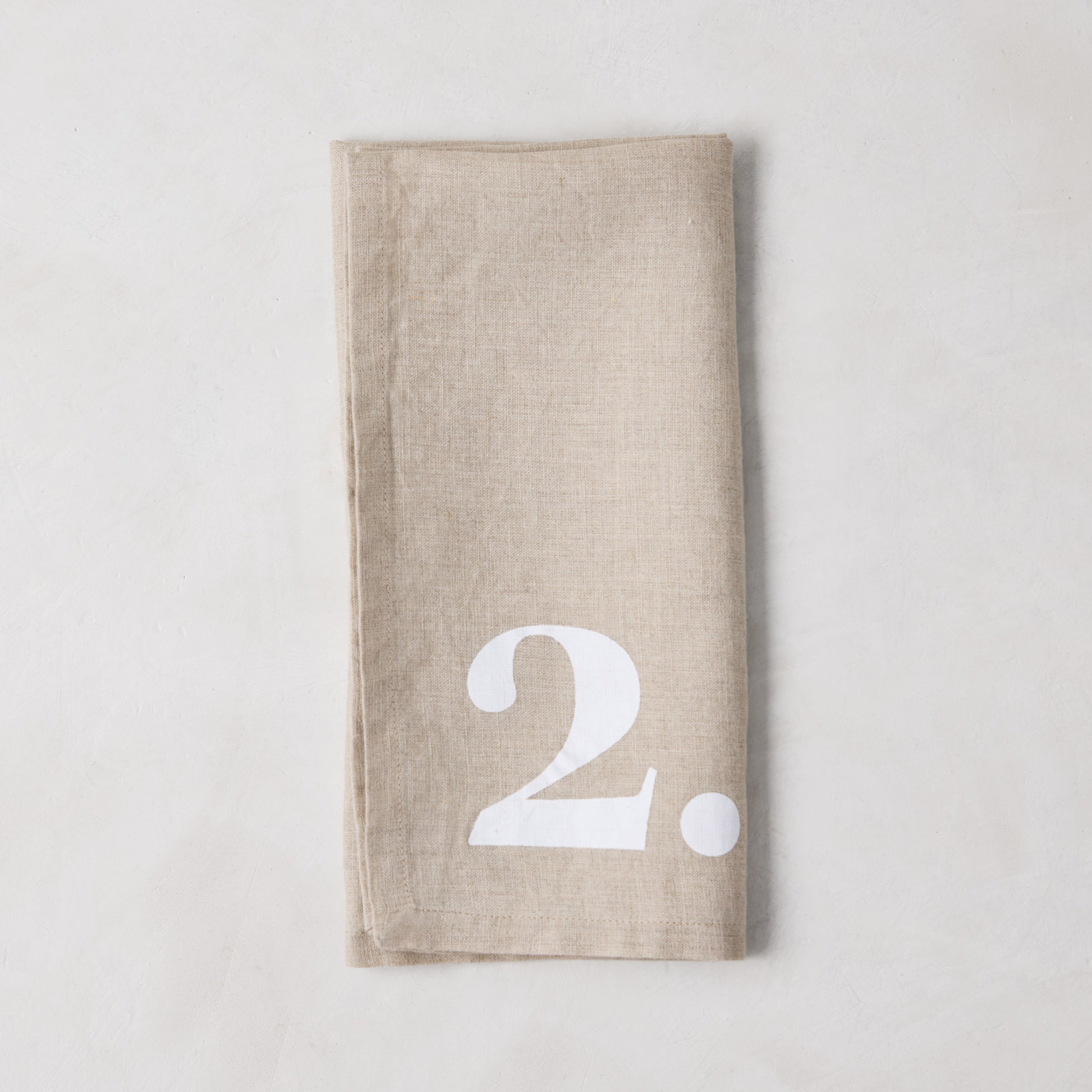 Diane Keaton + Hudson Grace Khaki Linen Numeric Napkin, folded, with a bold white number 2.