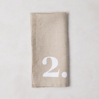 Diane Keaton + Hudson Grace Khaki Linen Numeric Napkin, folded, with a bold white number 2.