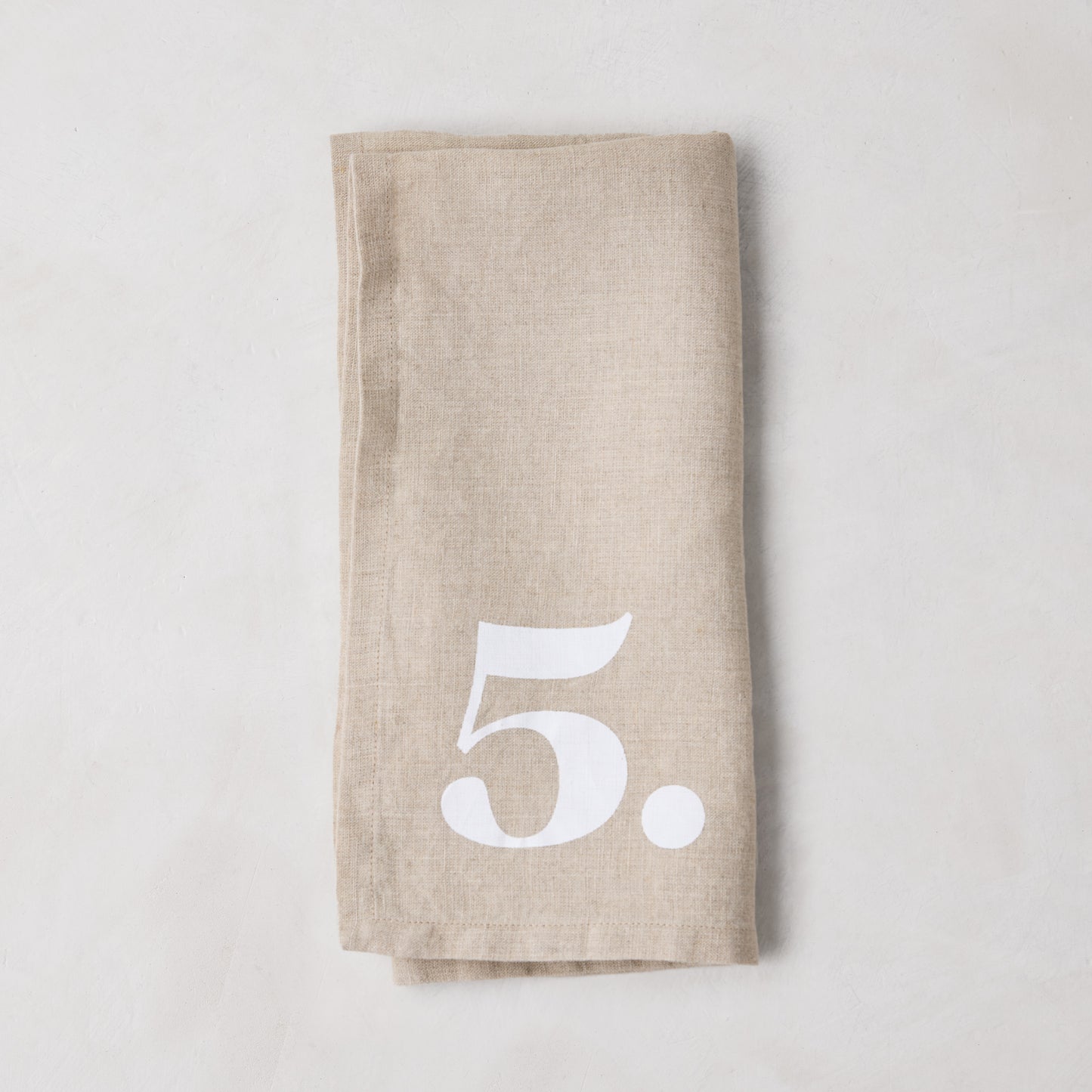 Diane Keaton + Hudson Grace Khaki Linen Numeric Napkin, folded, with a white number 5.
