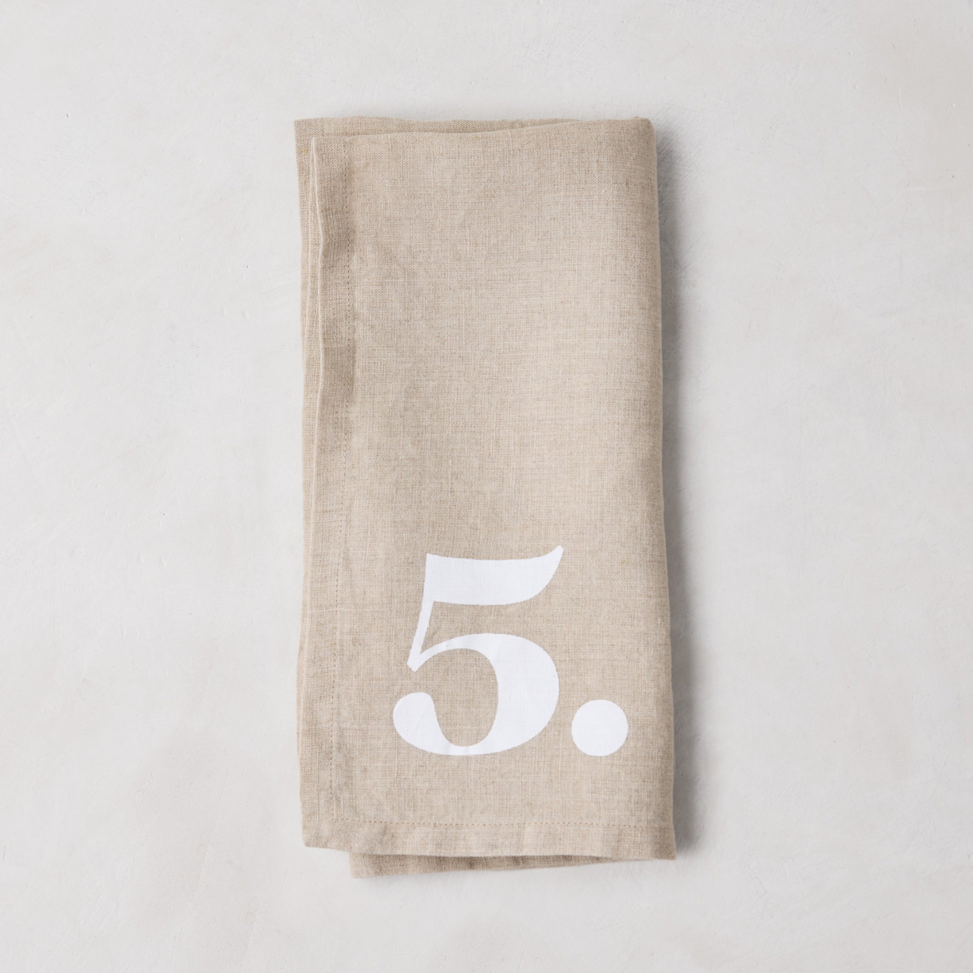 Diane Keaton + Hudson Grace Khaki Linen Numeric Napkin, folded, with a white number 5.