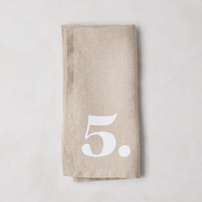 Diane Keaton + Hudson Grace Khaki Linen Numeric Napkin, folded, with a white number 5.