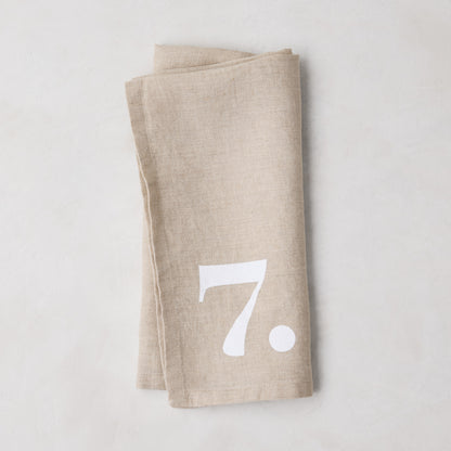 Diane Keaton + Hudson Grace Khaki Linen Numeric Napkin, folded, with a white number 7.