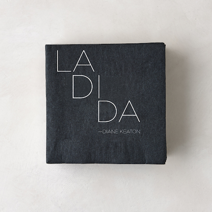 Black 3-ply paper cocktail napkin with "LA DI DA - DIANE KEATON" in white text.