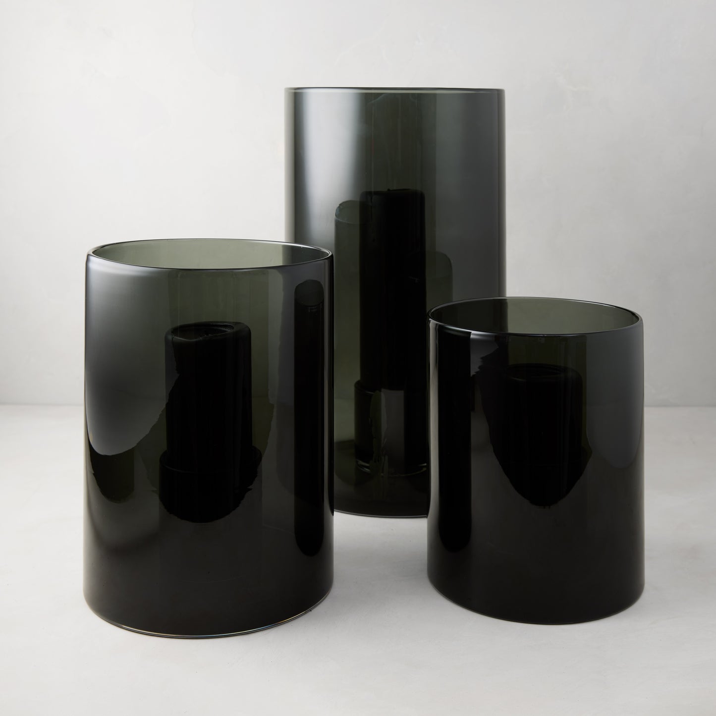 Three Diane Keaton + Hudson Grace smoke grey glass hurricanes, varying sizes.