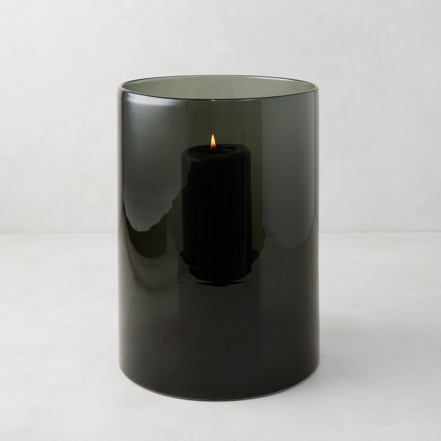 Medium Diane Keaton x Hudson Grace Smoke Grey Glass Hurricane with a lit black pillar candle.