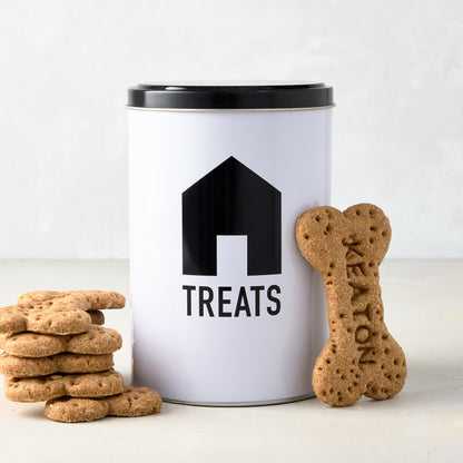 Diane Keaton x Hudson Grace white metal dog treat tin with black house icon, "TREATS" text, and black lid, next to dog biscuits.