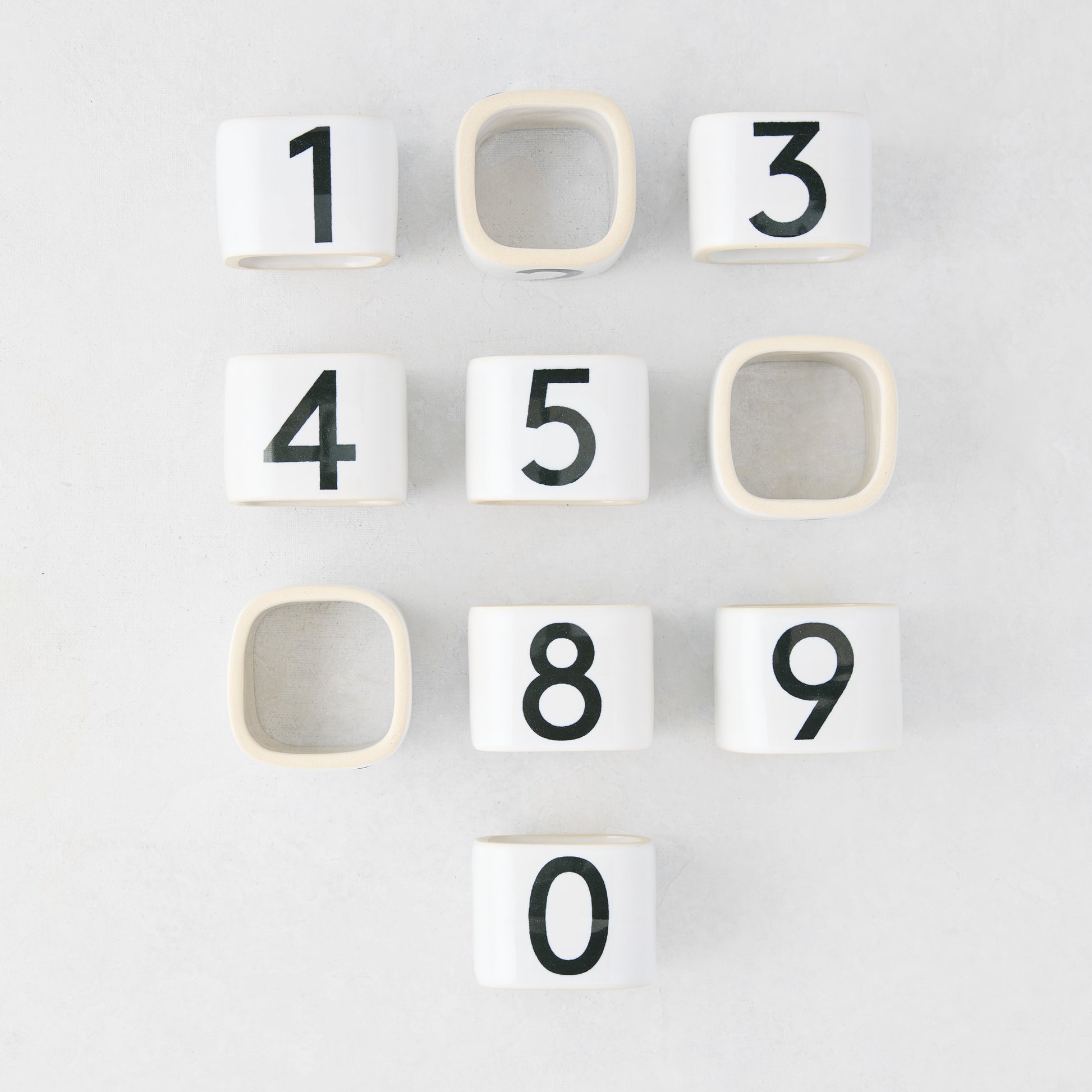 Diane Keaton + Hudson Grace white stoneware numeric napkin rings, numbered 0-9, on a light surface.