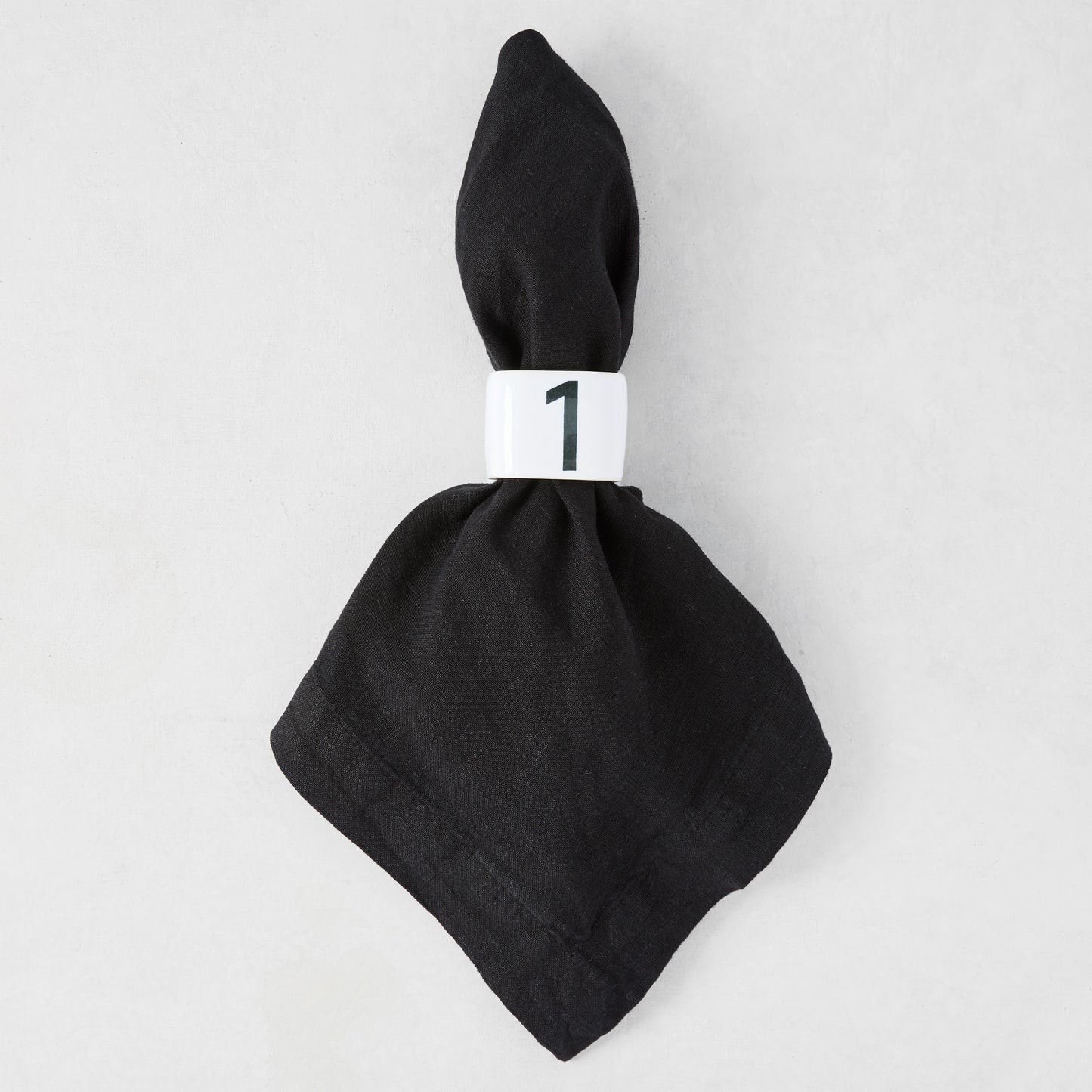 Diane Keaton + Hudson Grace white stoneware numeric napkin ring "1" on a black linen napkin.