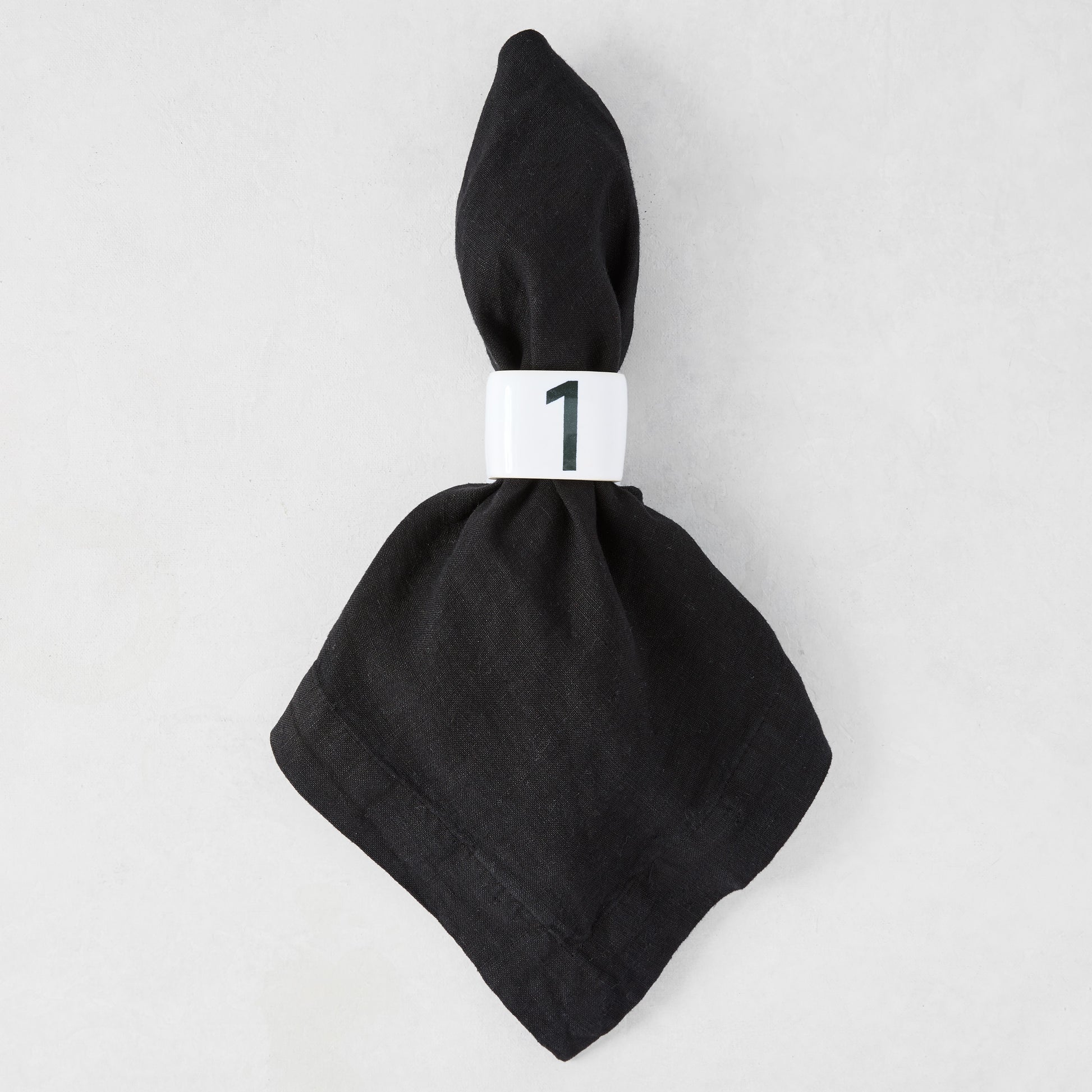Diane Keaton + Hudson Grace white stoneware numeric napkin ring "1" on a black linen napkin.