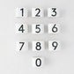 Set of 10 white stoneware napkin rings with black numbers 0-9, from the Diane Keaton + Hudson Grace Collection.