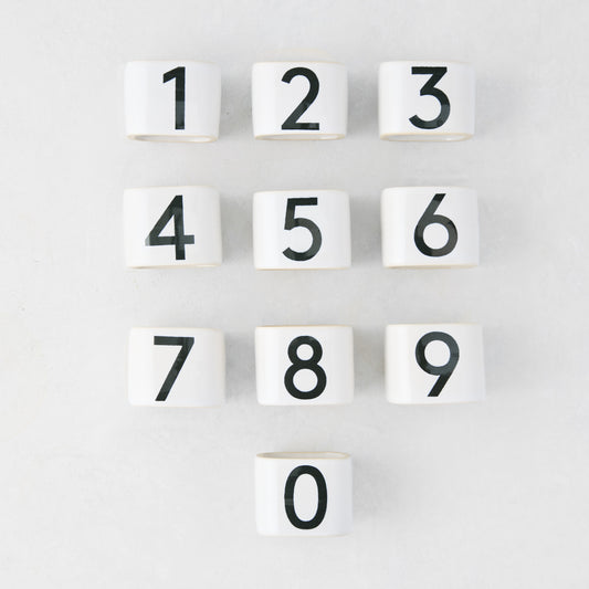 Set of 10 white stoneware napkin rings with black numbers 0-9, from the Diane Keaton + Hudson Grace Collection.