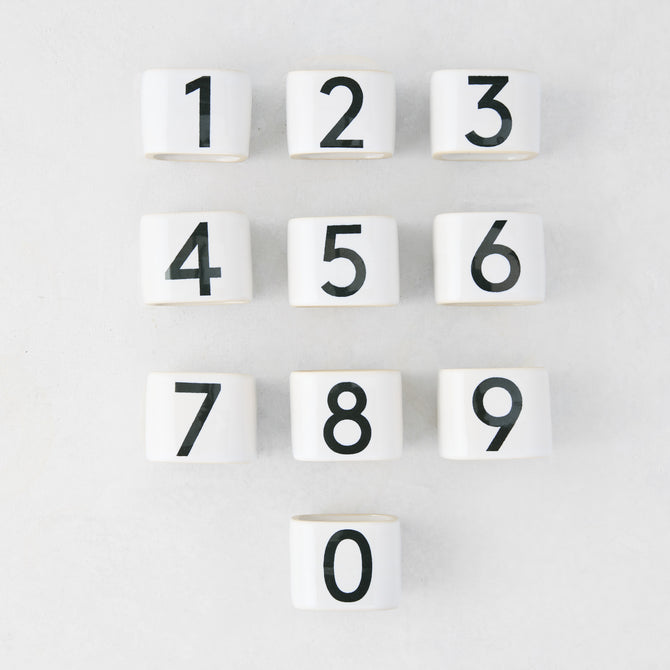 Set of 10 white stoneware napkin rings with black numbers 0-9, from the Diane Keaton + Hudson Grace Collection.