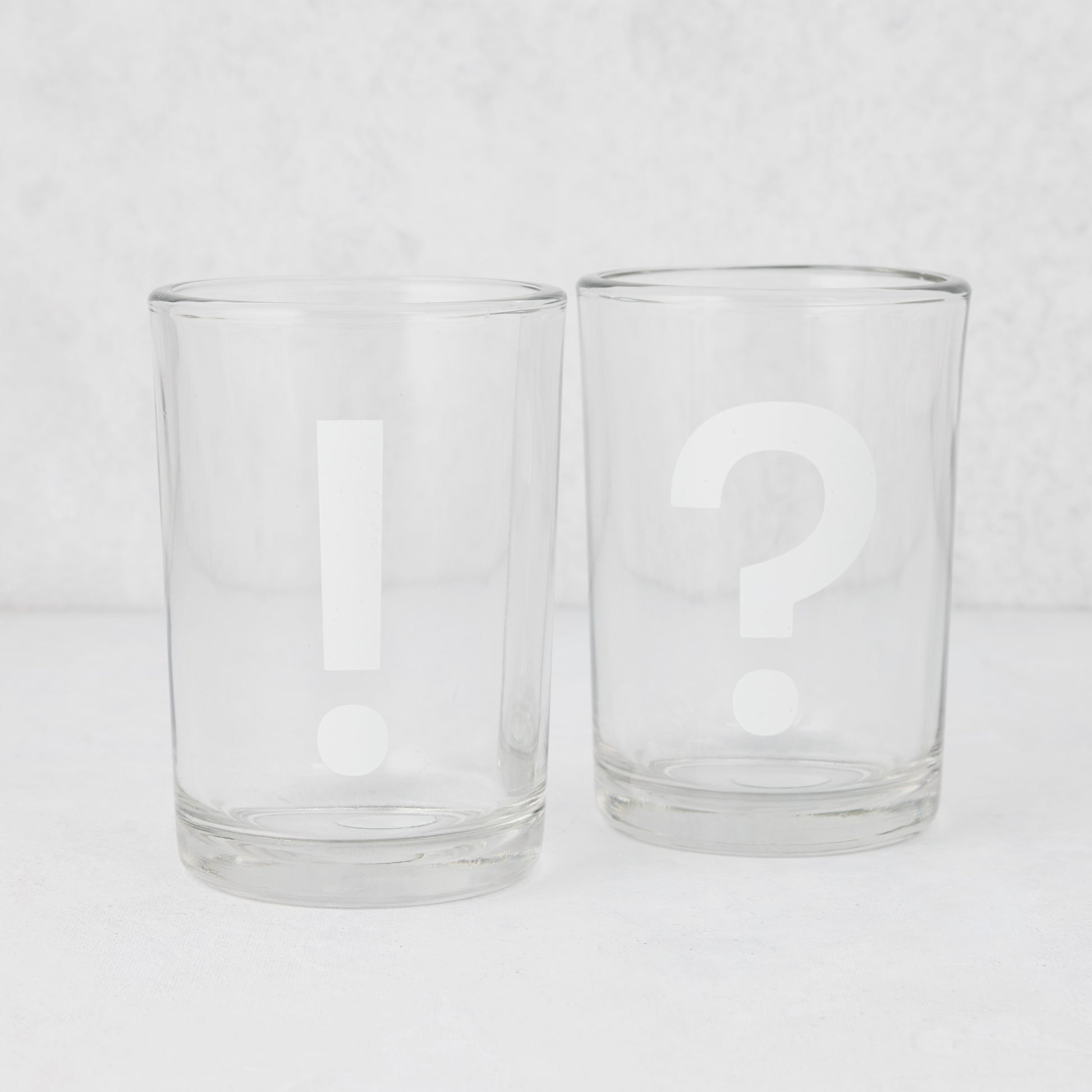 Two clear glass tumblers, one with a white exclamation mark, the other with a white question mark.