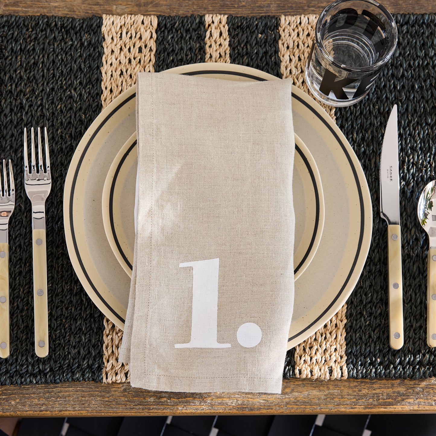 Diane Keaton + Hudson Grace Sketch Stoneware Dinner Plate with black line detail, beige napkin, and cutlery.