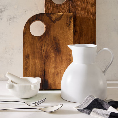White ceramic pitcher, marble mortar and pestle, wooden cutting boards, and checkered napkin.