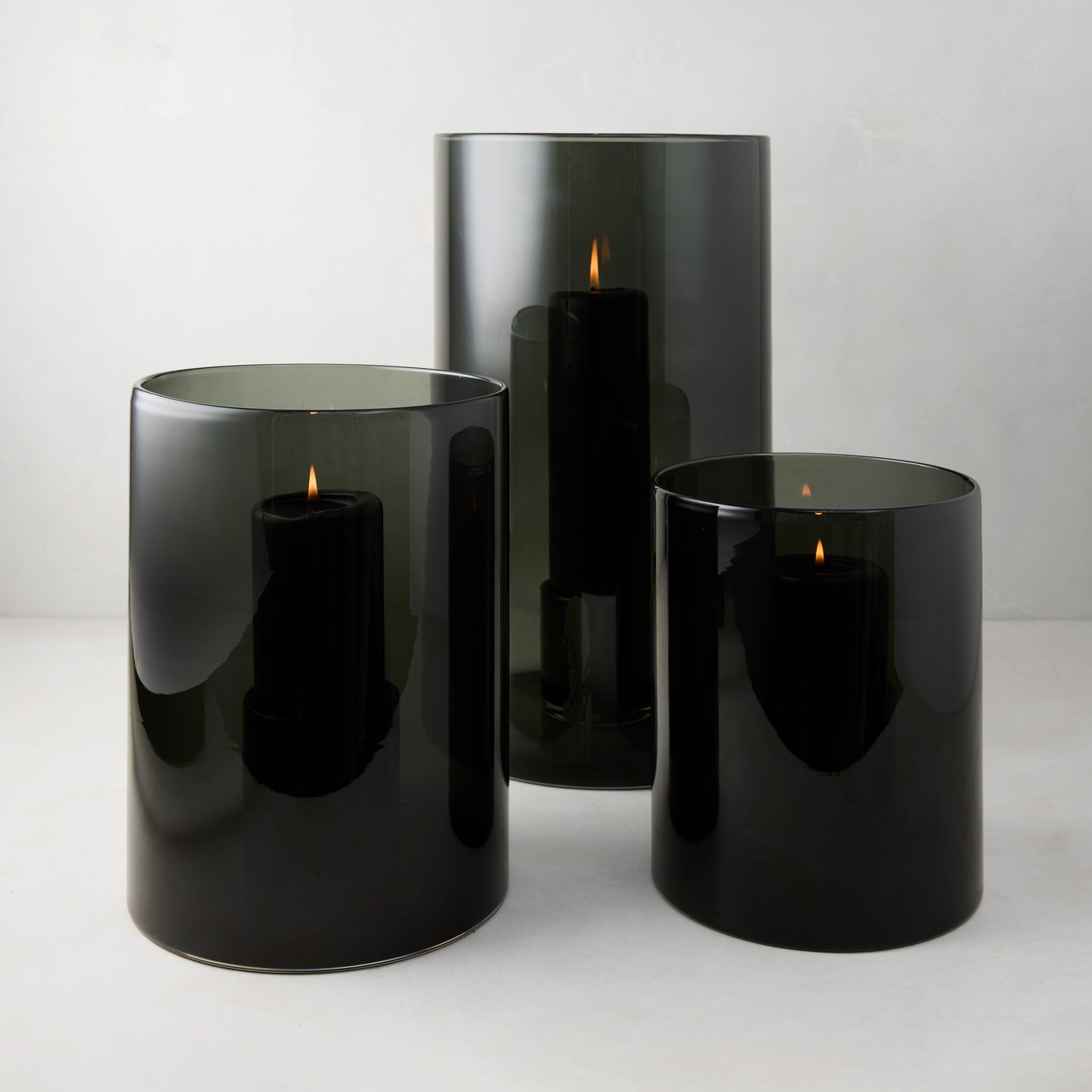 Three Diane Keaton + Hudson Grace smoke grey glass hurricanes with lit black pillar candles.