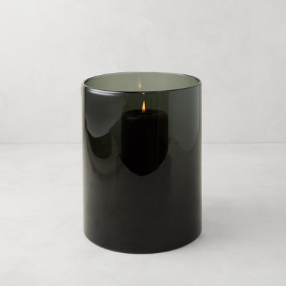 Small Smoke Grey Glass Hurricane from Diane Keaton + Hudson Grace, with a lit black pillar candle inside.