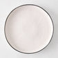 Diane Keaton + Hudson Grace Studio black rim stoneware dinner plate, irregular shape, textured white base.