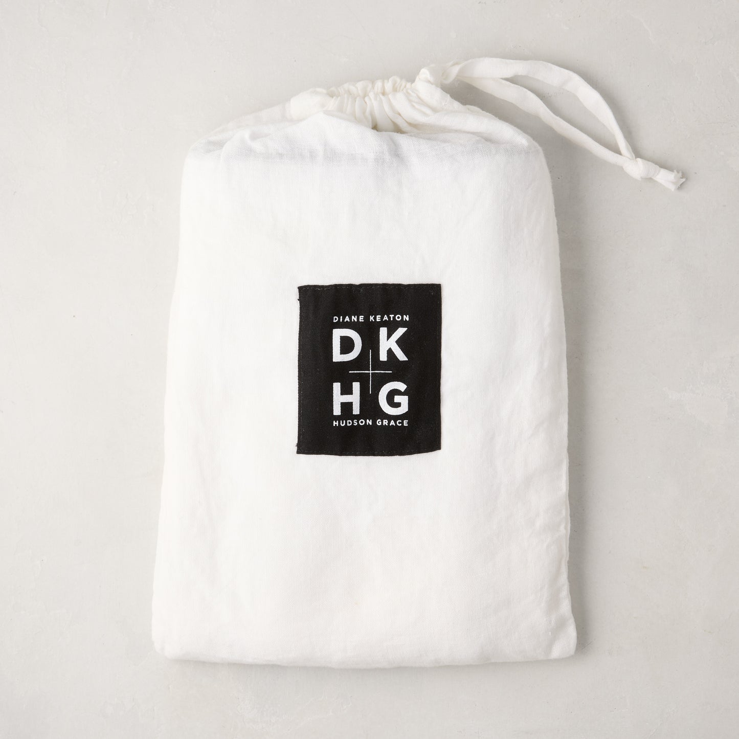 White washed linen drawstring bag with a black "Diane Keaton DKHG Hudson Grace" label.