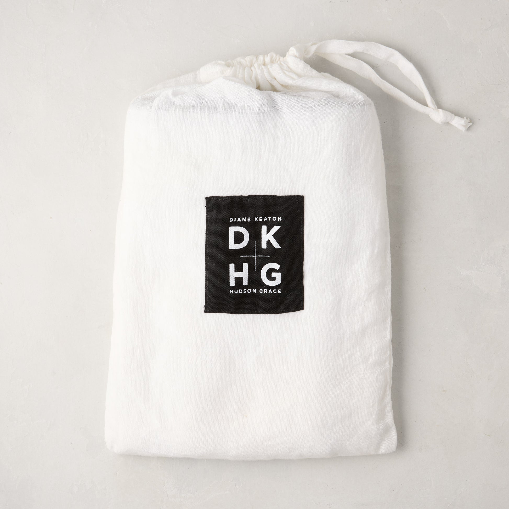 White washed linen drawstring bag with a black "Diane Keaton DKHG Hudson Grace" label.