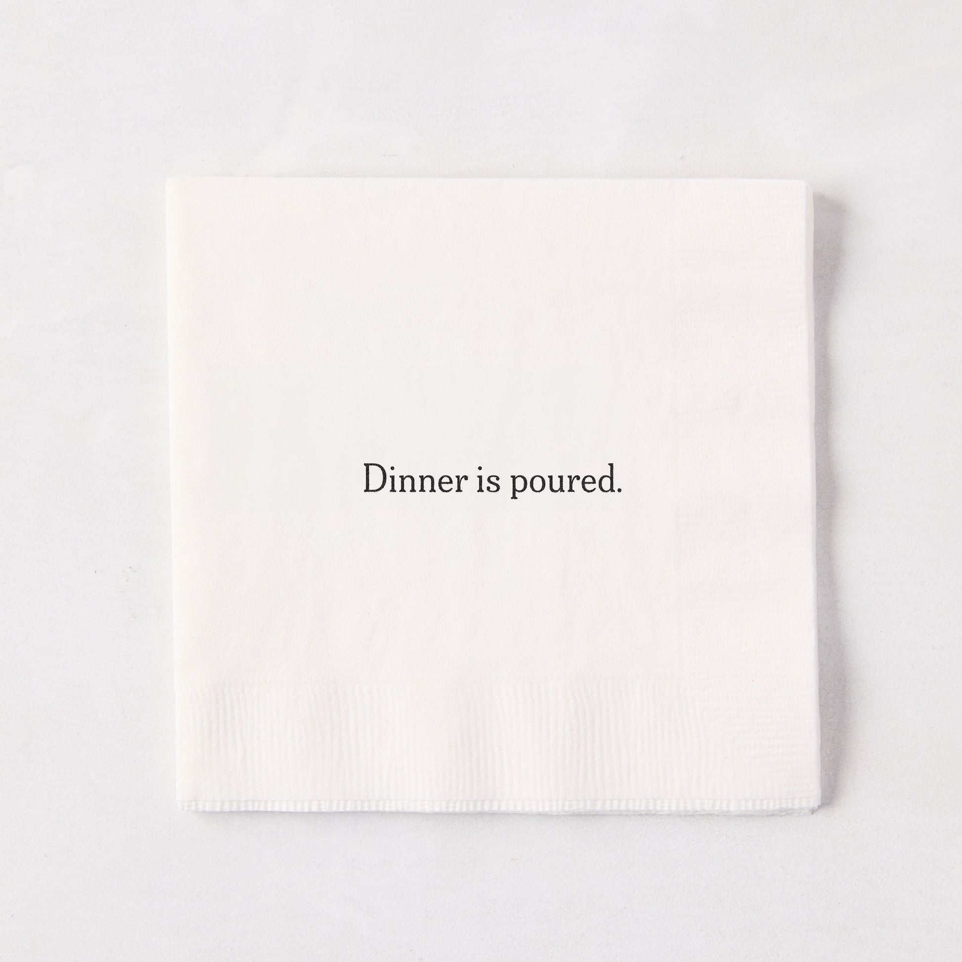 White 5.5" square paper cocktail napkin with "Dinner is poured." in black text.