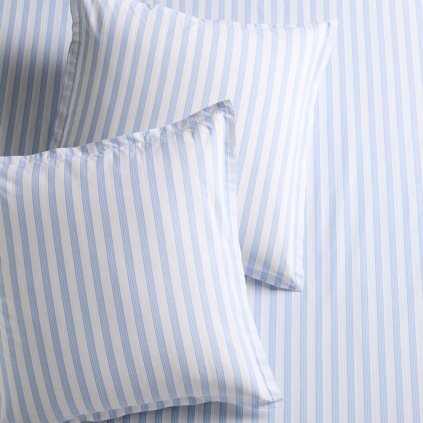 Two Dobby Blue Stripe Cotton Euro Shams with subtle texture, on a matching striped sheet.