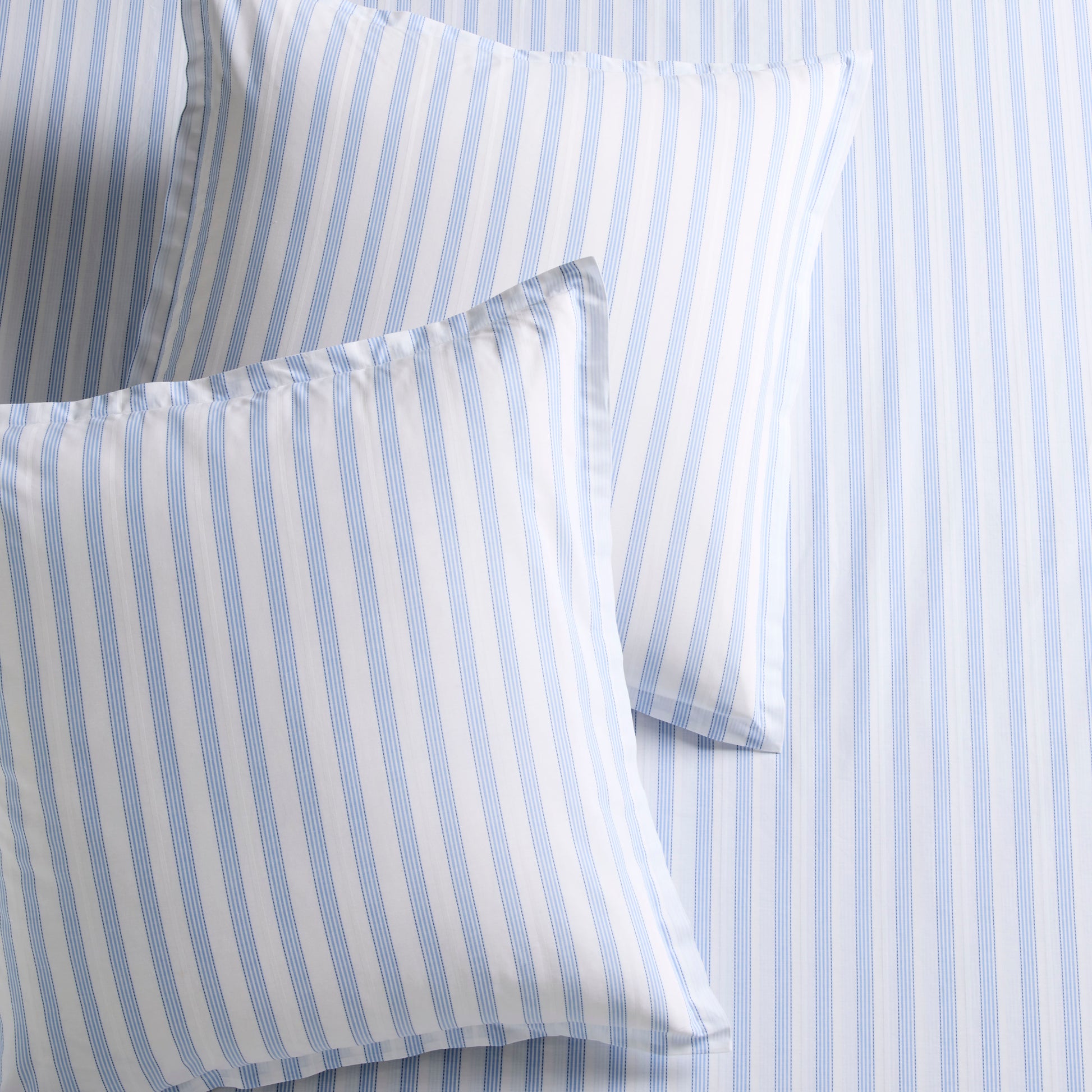 Two Dobby Blue Stripe Cotton Euro Shams with subtle texture, on a matching striped sheet.