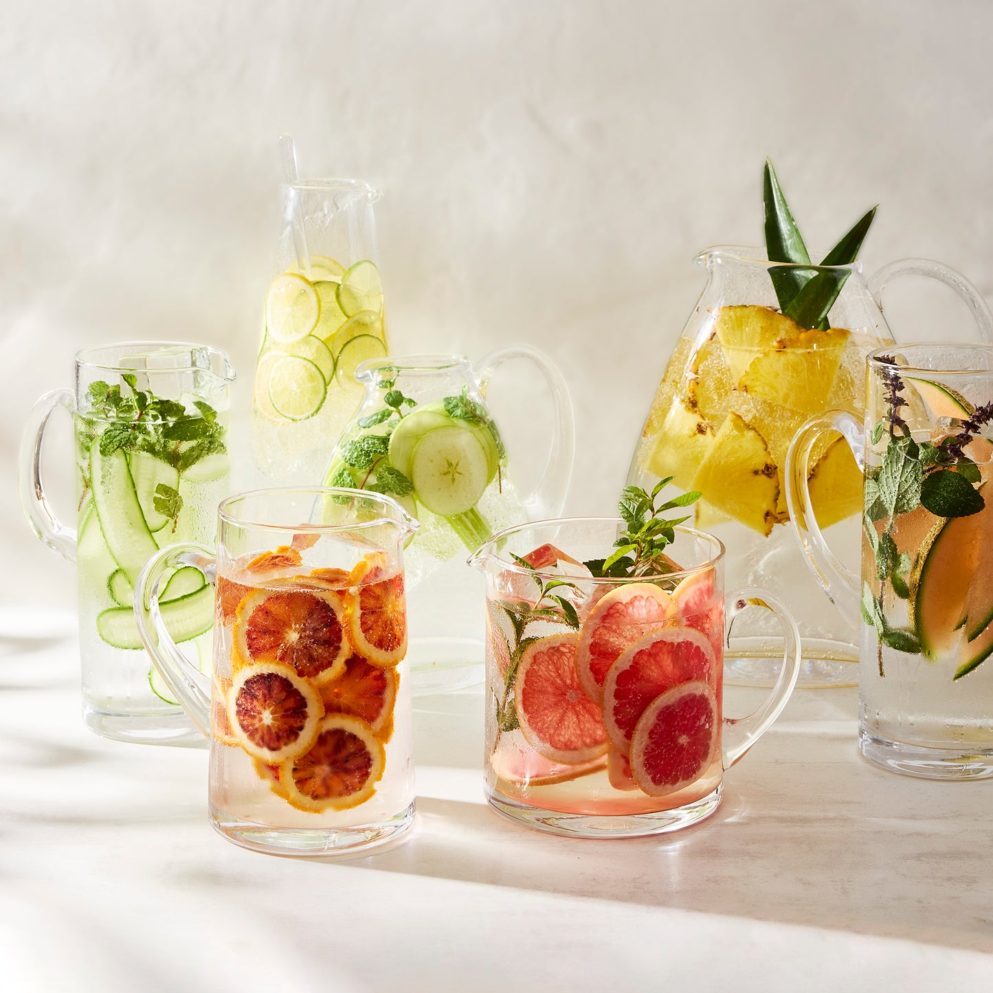 Clear glass bar pitchers and carafes filled with fruit-infused water, including citrus, cucumber, and pineapple.