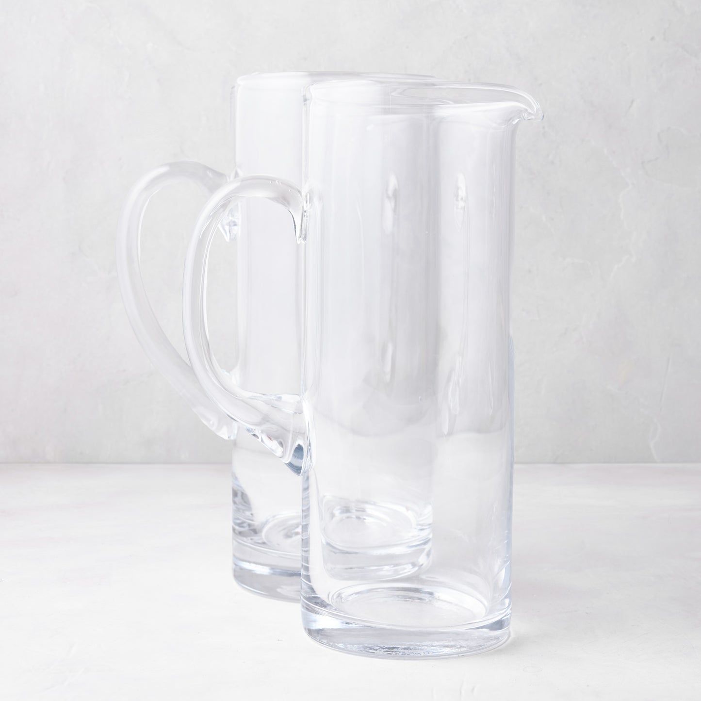 Two clear glass Downtown Tall Bar Pitchers, one with a handle, on a white surface.
