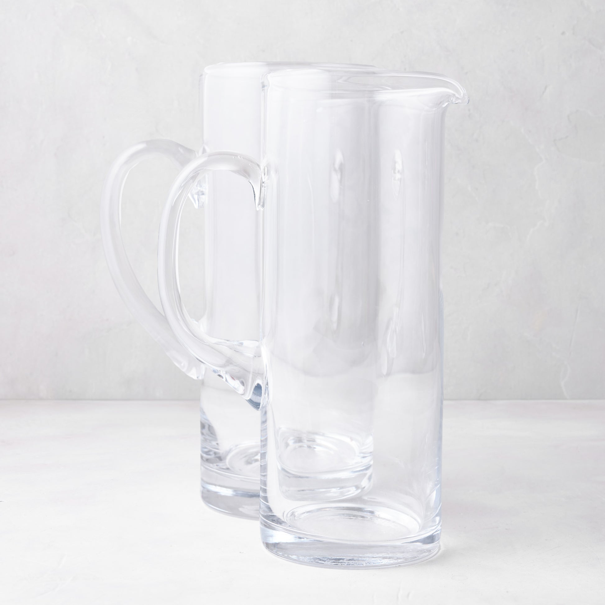 Two clear glass Downtown Tall Bar Pitchers, one with a handle, on a white surface.