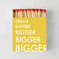 Oversized "Dream Bigger" matches in a yellow box with white text, showing red-tipped wooden matchsticks.