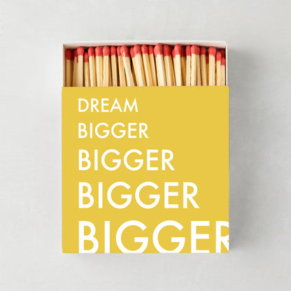 Oversized "Dream Bigger" matches in a yellow box with white text, showing red-tipped wooden matchsticks.