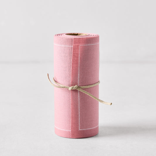 Dusty pink tear-off cotton cocktail napkin roll with white stitching, tied with twine.