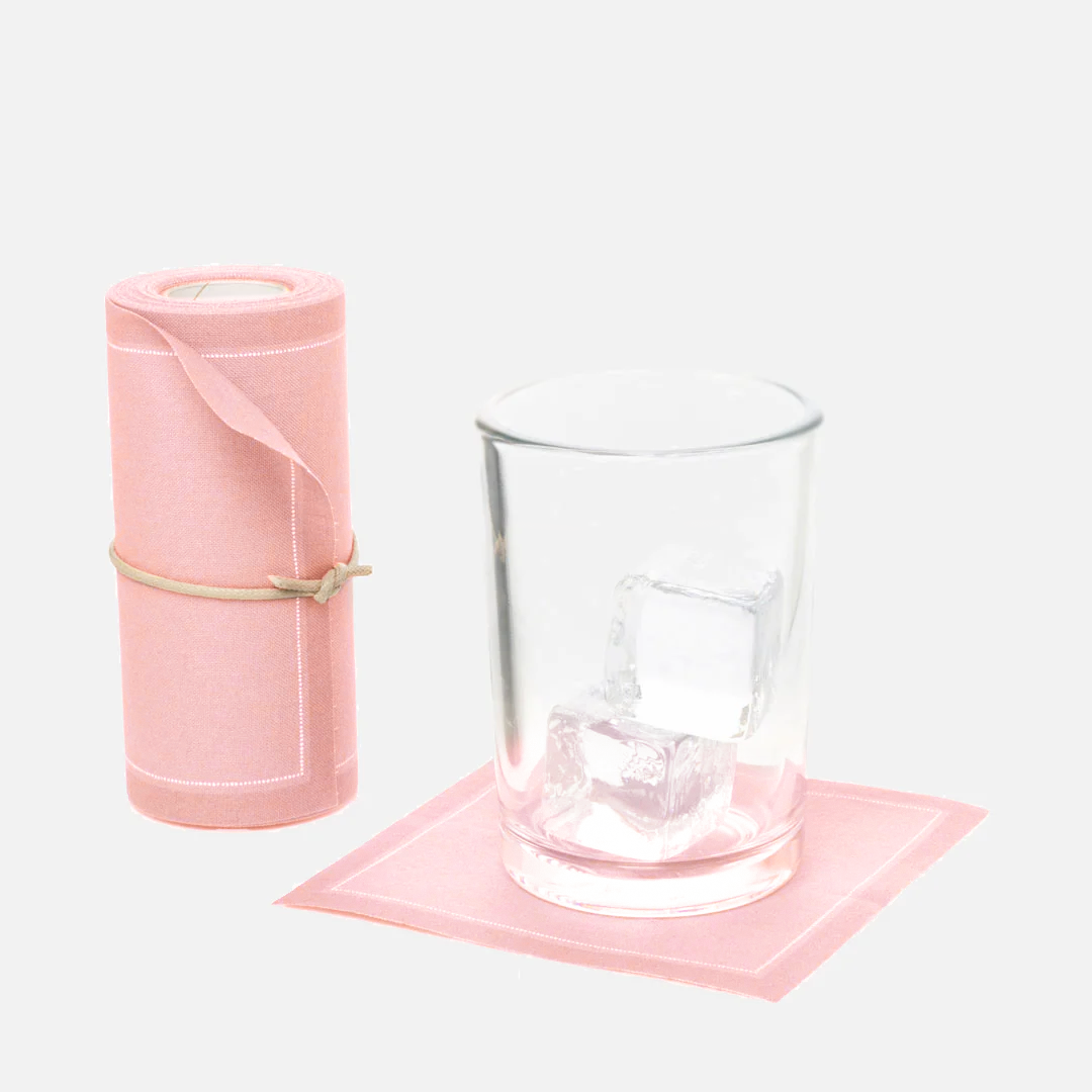 Dusty pink tear-off cotton cocktail napkin roll, with one napkin under a glass with ice.