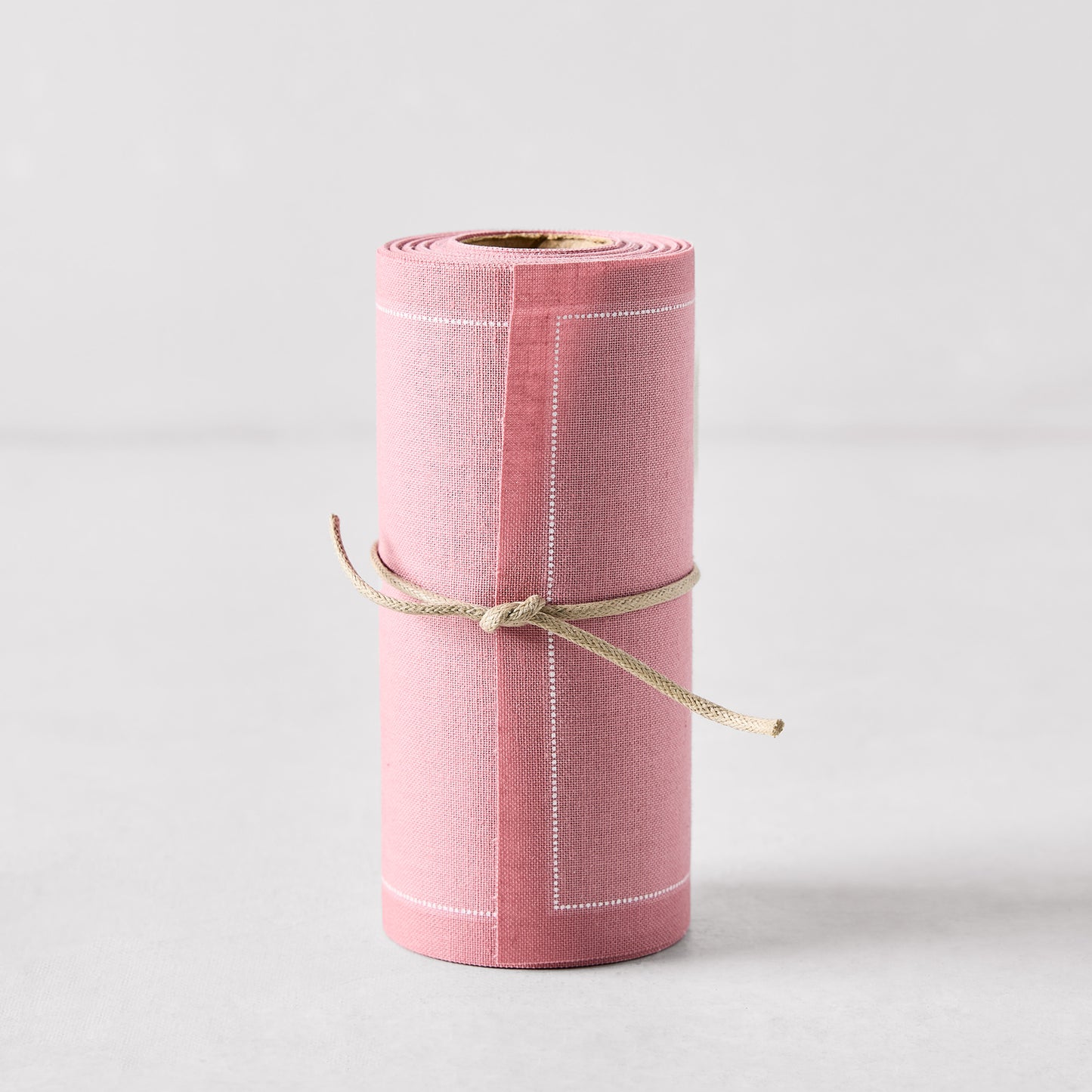 Dusty pink tear-off cotton cocktail napkin roll with white stitching, tied with twine.