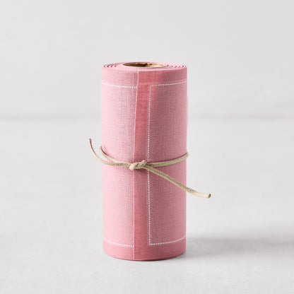 Dusty pink tear-off cotton cocktail napkin roll with white stitching, tied with twine.
