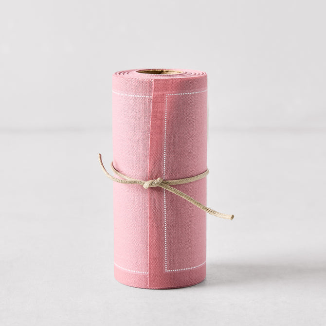 Dusty pink tear-off cotton cocktail napkin roll with white stitching, tied with twine.