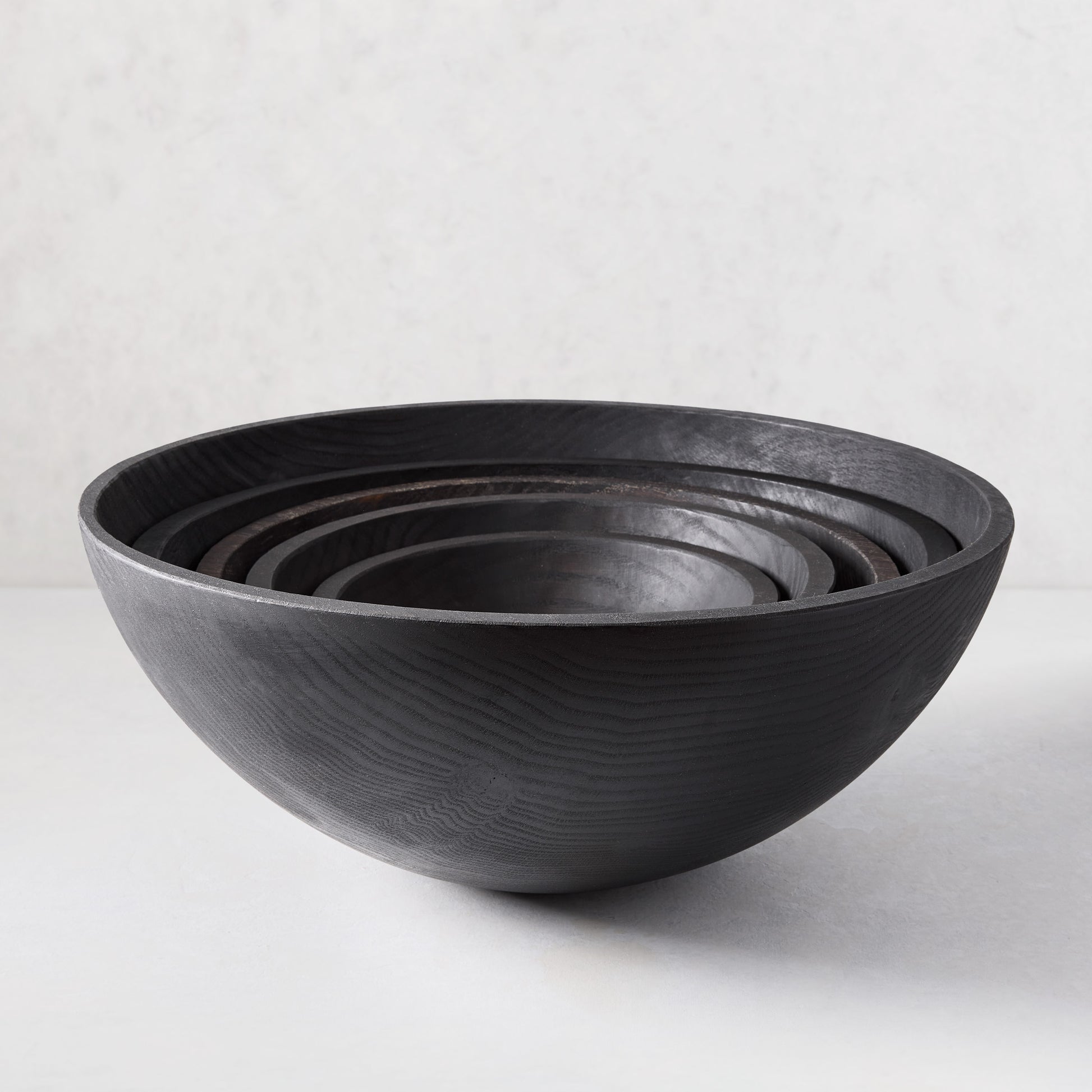 Set of four nested ebonized wood bowls, dark finish highlighting wood grain, 15" largest.